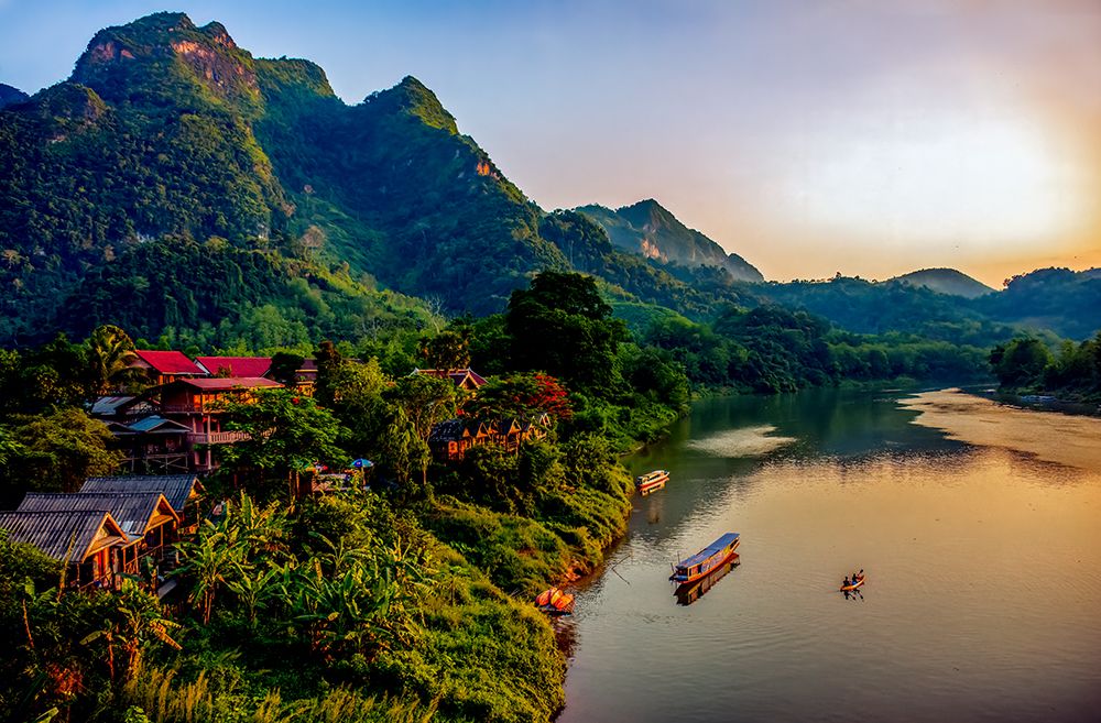 Mekong River village, Laos. Mountain village at sunset lighting river and mountains. art print by Murray McCallum for $57.95 CAD