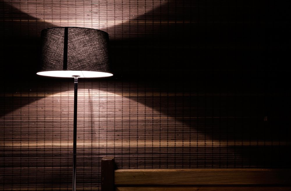 A Modern Floor Lamp Illuminates A Dark, Textured Wall Above A Wooden Bench. art print by Gabriel Roveda for $57.95 CAD