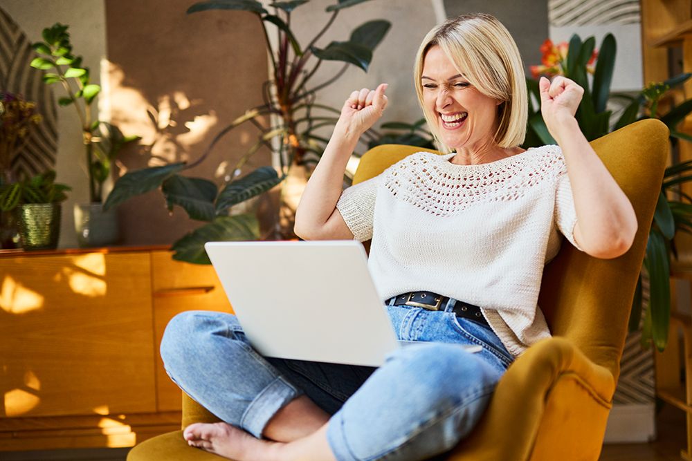 Cheerful Woman Sitting In Armchair At Home Celebrating Laptop Success art print by Bartek Szewczyk for $57.95 CAD