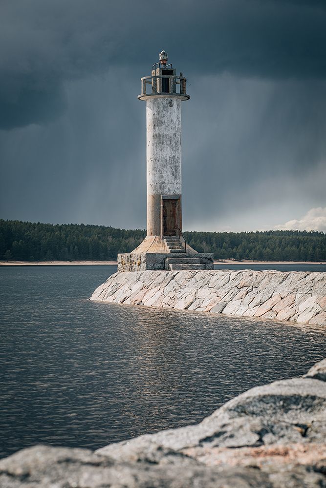 Lighthouse Standing Against Storm Clouds On Rocky Breakwater art print by Kseniia Liubasova for $57.95 CAD