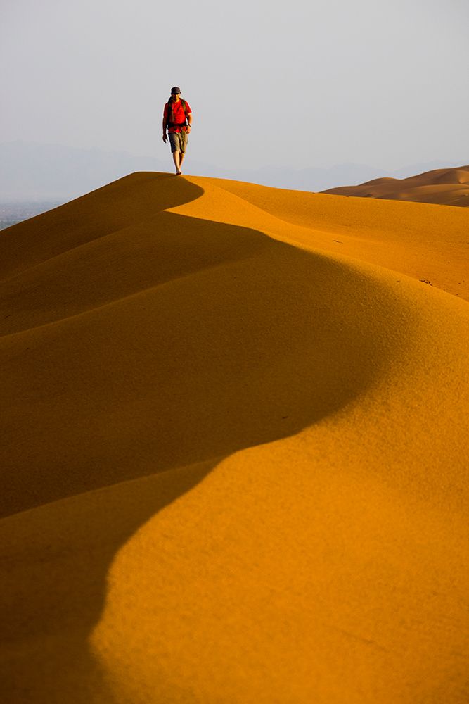 Male Hiking In Red / Orange Sand Dunes In Desert. art print by Gabe Rogel for $57.95 CAD