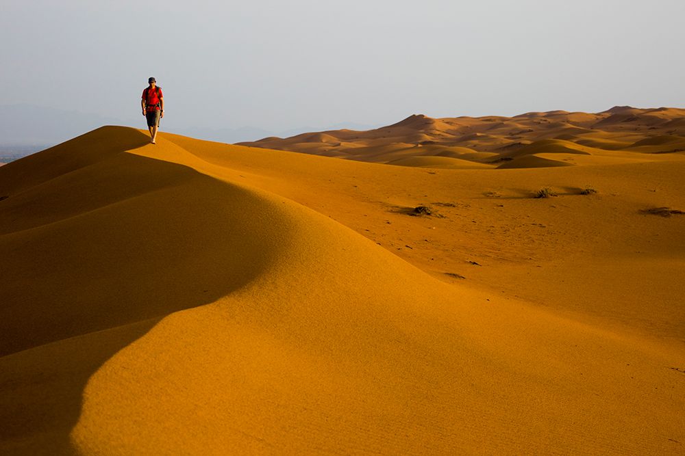 Male Hiking In Red / Orange Sand Dunes In Desert. art print by Gabe Rogel for $57.95 CAD