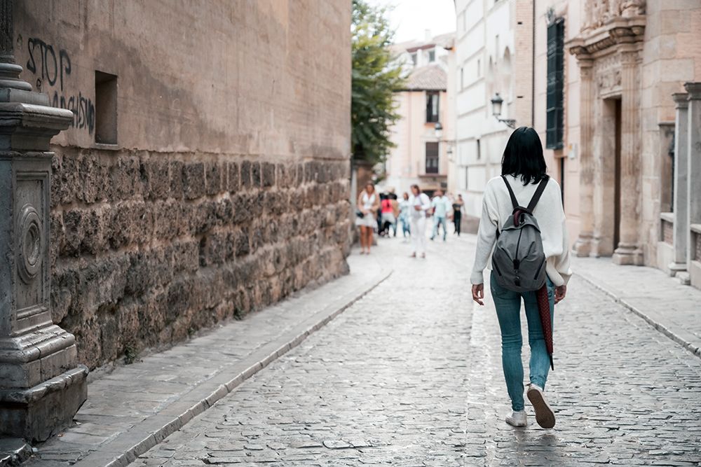 Woman With Backpack Walking On Cobblestone Street Alone art print by Rafa Fernandez for $57.95 CAD