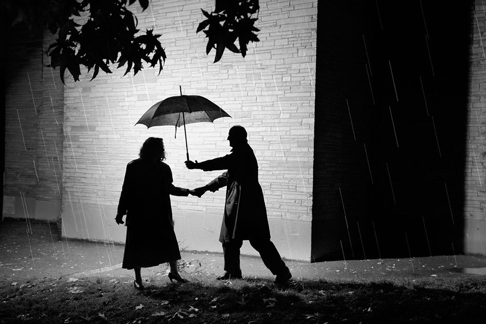 A Man Invites A Woman To Share His Umbrella As They Walk Outside In The Rain. art print by Ethan Welty for $57.95 CAD