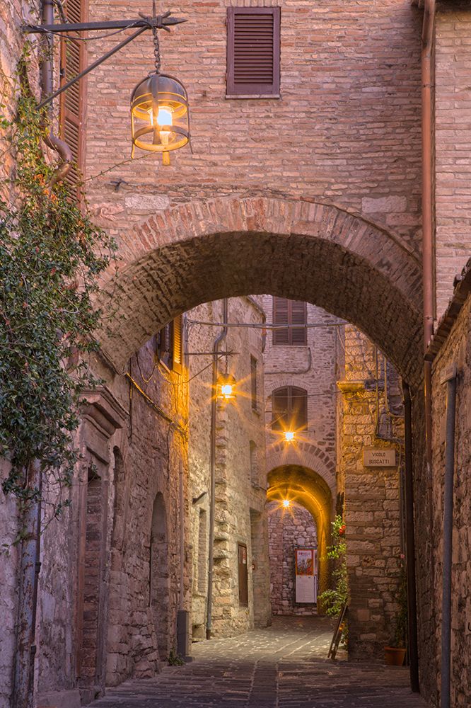 Italy- Umbria- Assisi. Alleyway with arches and lanterns in the evening. art print by Julie Eggers for $57.95 CAD